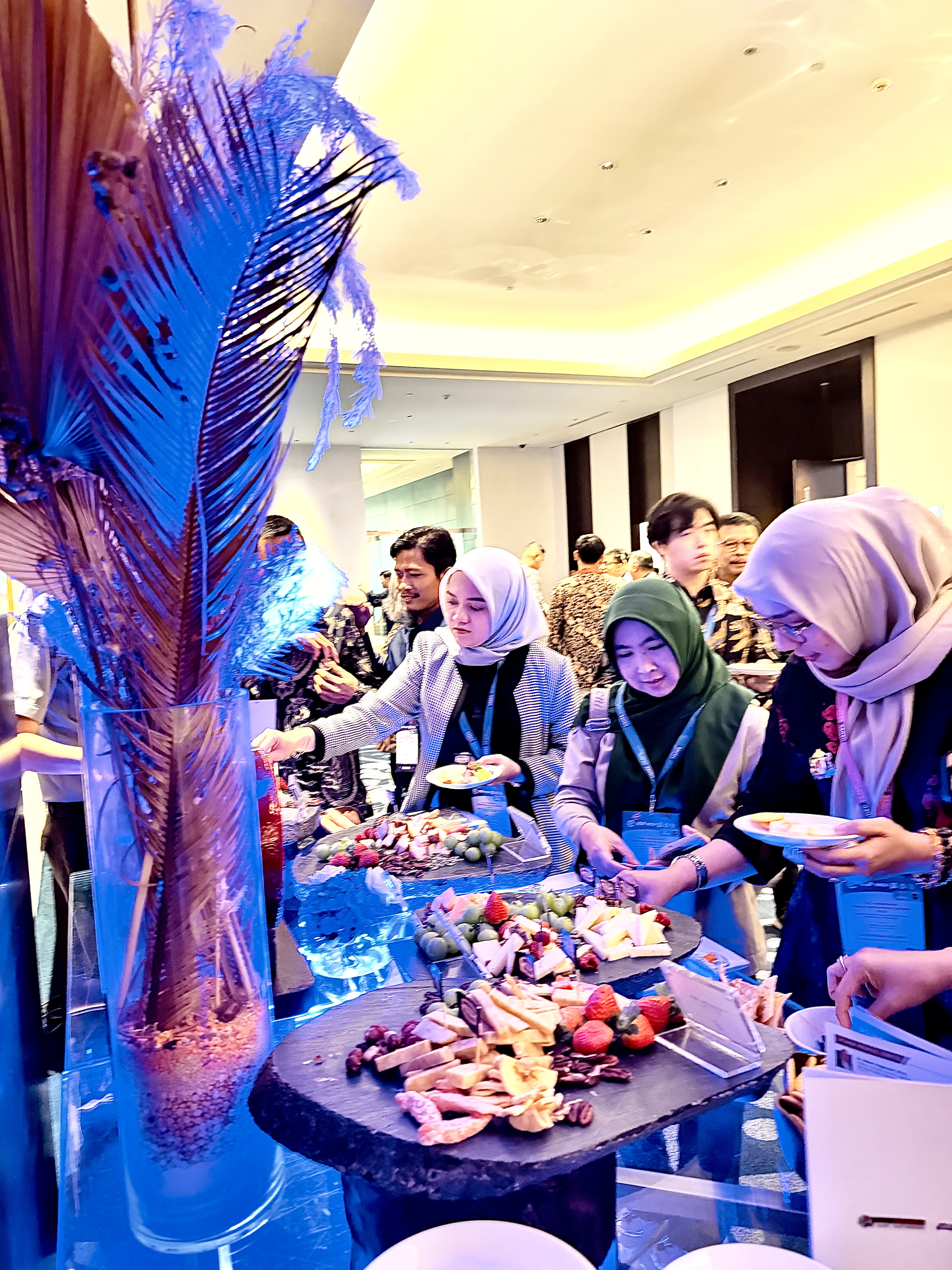 People select from various charcuterie boards on a blue-lit table and load their plates with cheese, sausage, and fruit.