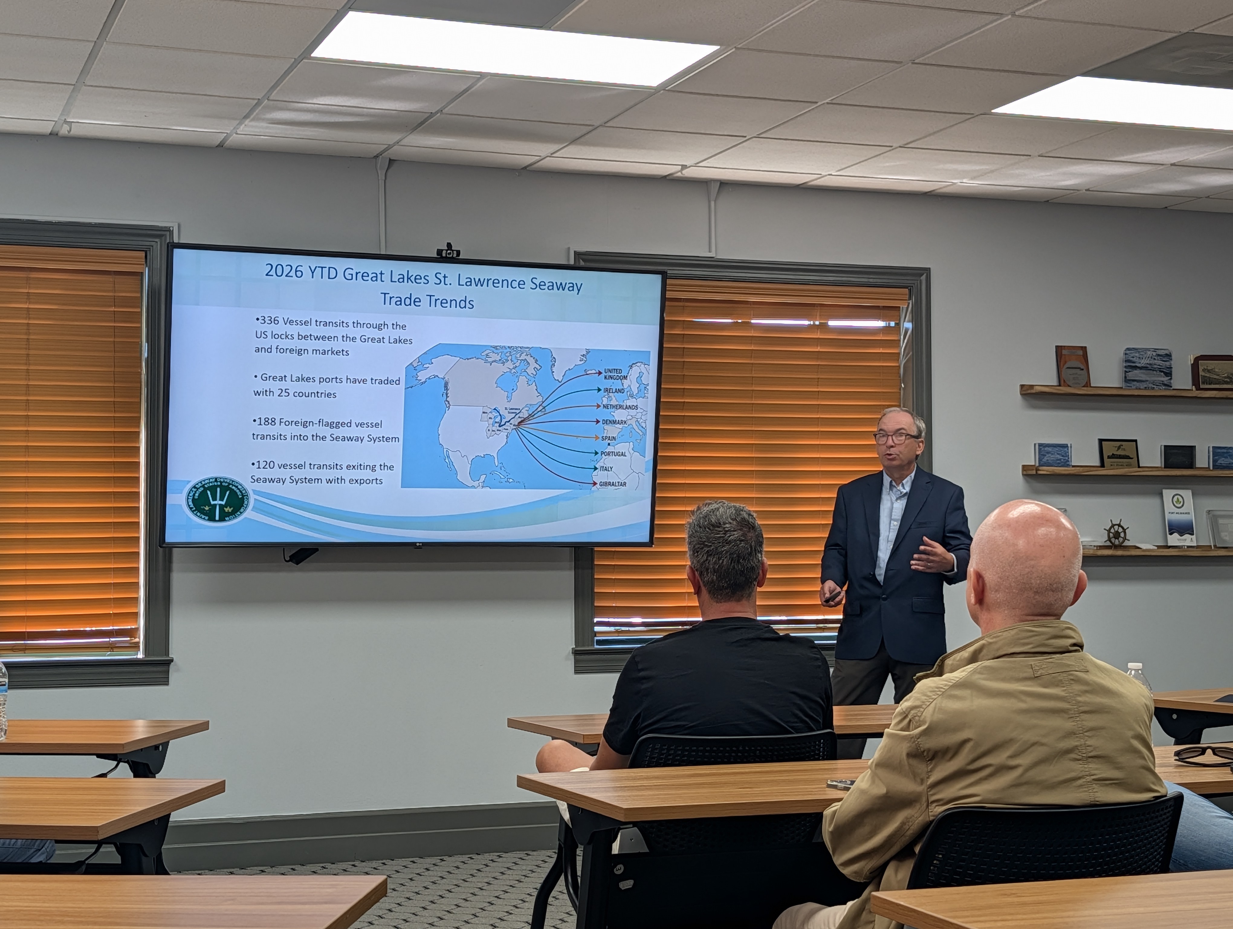 Man leads presentation at front of a room. The presentation is on the Great Lakes trade trends.