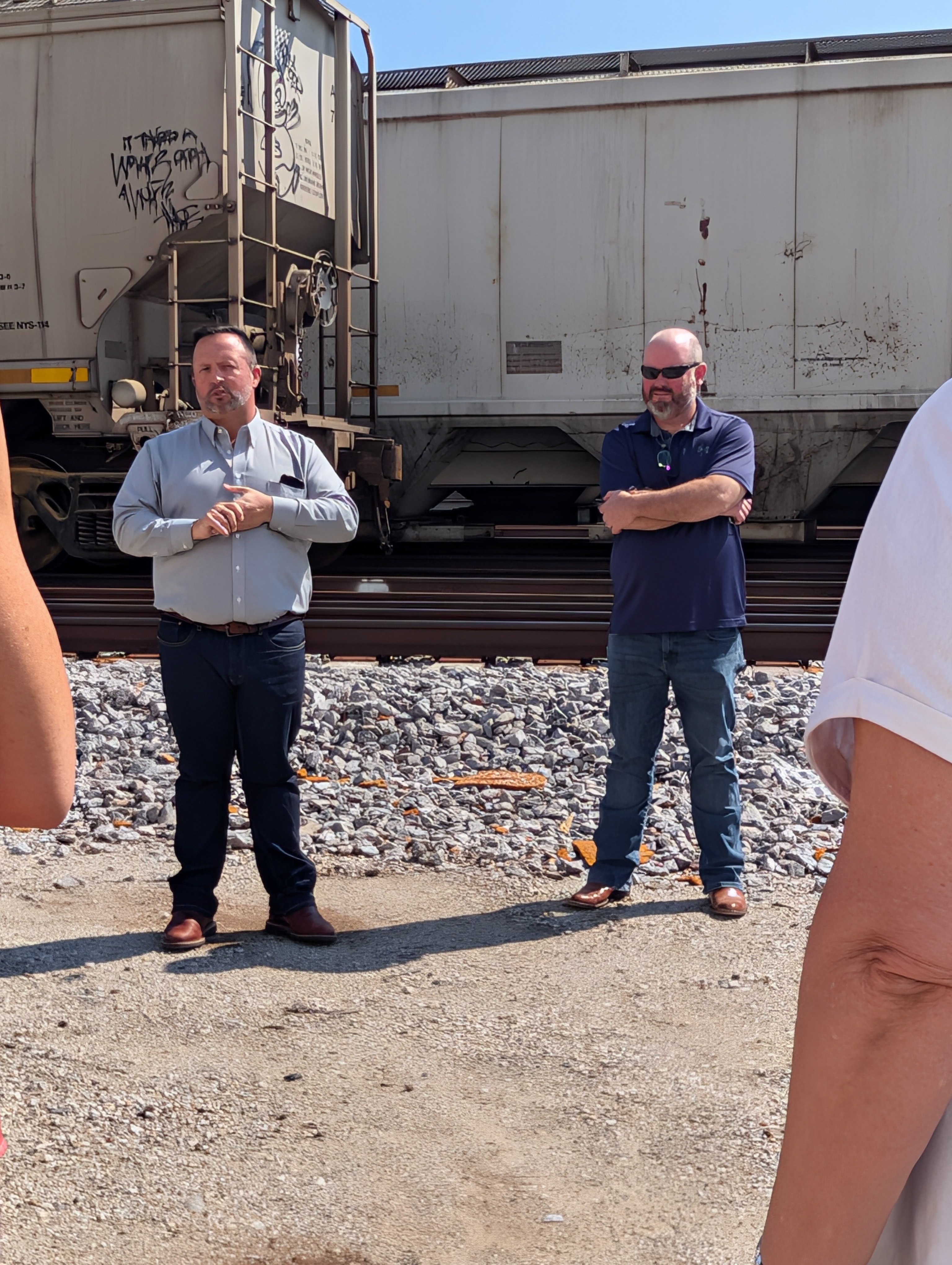 Two men speak to the group with the trains in the background.