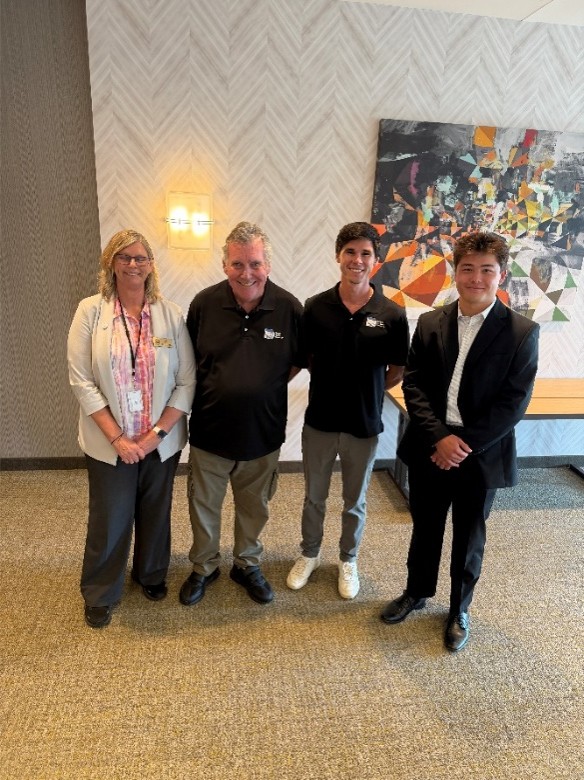 Four people smile and pose for photo in the presentation room.