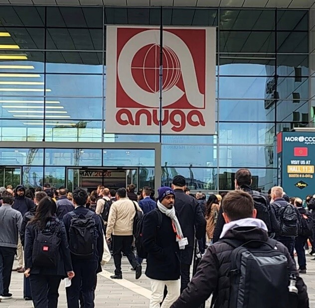 Crowds walking in front of a glass building with the ANUGA logo on it.